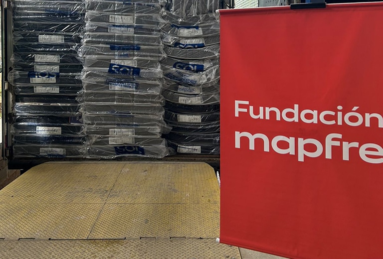 Ajuda humanitária Grupo de voluntários da Fundación Mapfre posando para foto em galpão de armazenamento, vestindo camisetas brancas com a inscrição "Voluntários Fundación Mapfre", durante ação de apoio às famílias atingidas pelas chuvas em Juiz de Fora, Minas Gerais.